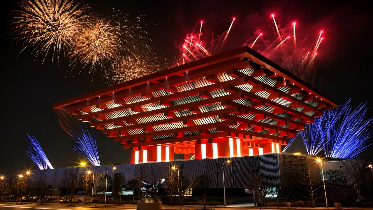 力方国际数字设计上海世博会项目夜景照片，红色大型展馆建筑在烟花与蓝紫色灯光映衬下亮起